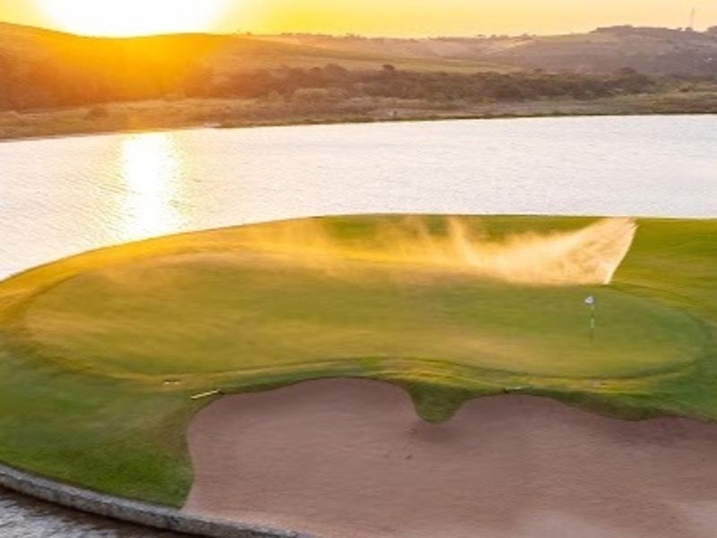Scenic aerial view of a golf course green featuring a sand bunker and lake at sunset.