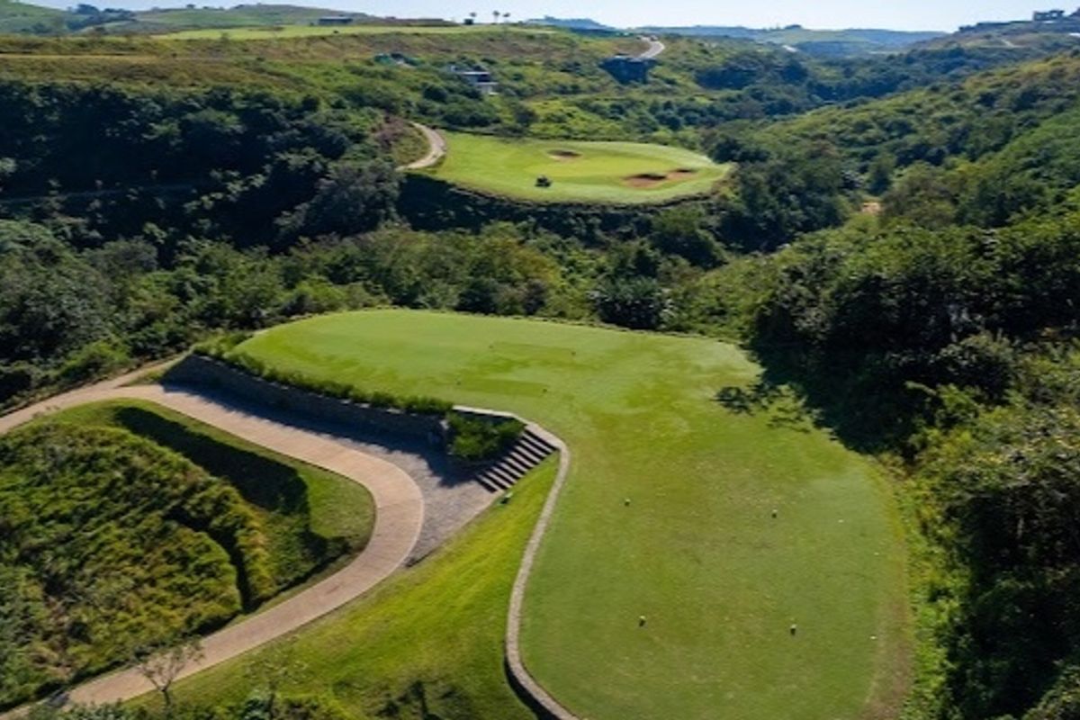 Aerial view of a well-maintained golf course fairway and green, featuring paved cart paths and natural landscaped terrain.