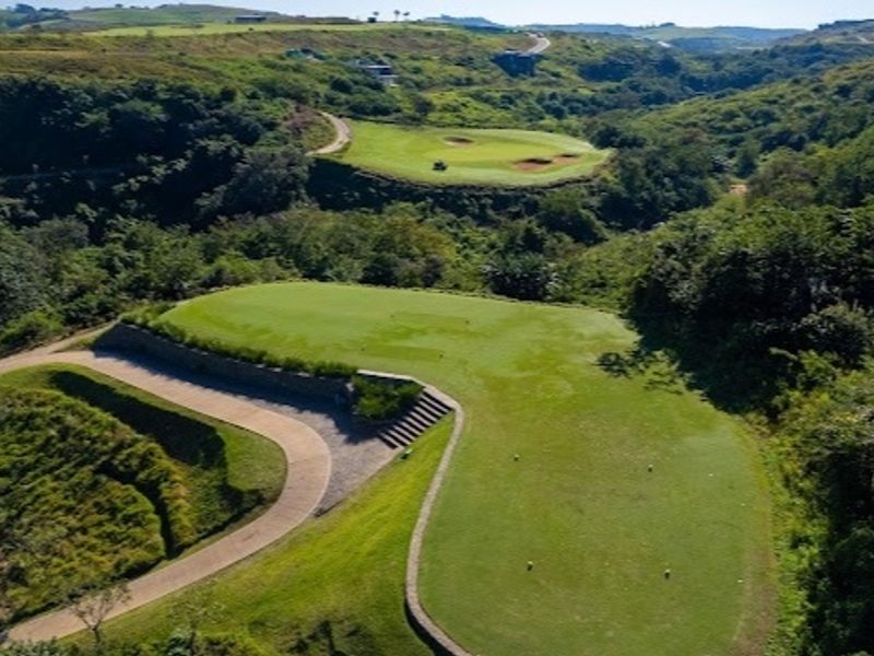 Aerial view of a well-maintained golf course fairway and green, featuring paved cart paths and natural landscaped terrain.