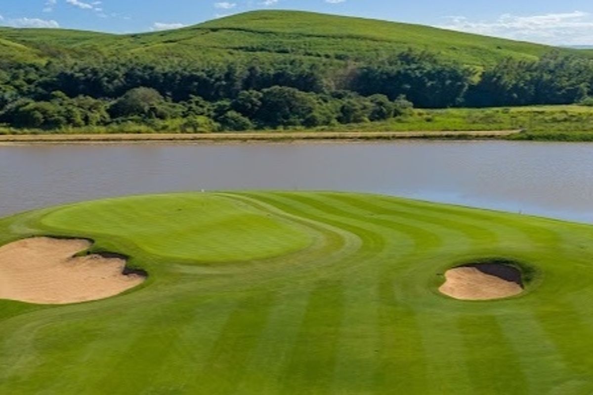Scenic aerial view of a manicured golf course green featuring sand bunkers and a tranquil lake backdrop.