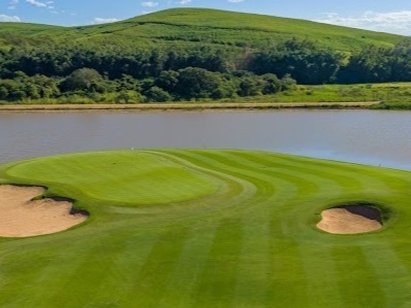 Scenic aerial view of a manicured golf course green featuring sand bunkers and a tranquil lake backdrop.