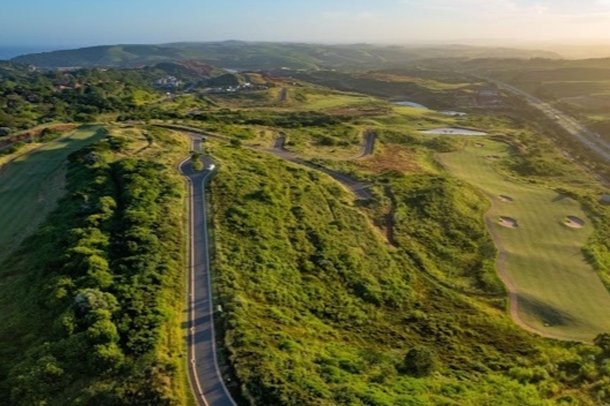 An aerial view of a residential estate featuring a paved road winding through landscaped hills and a golf course.
