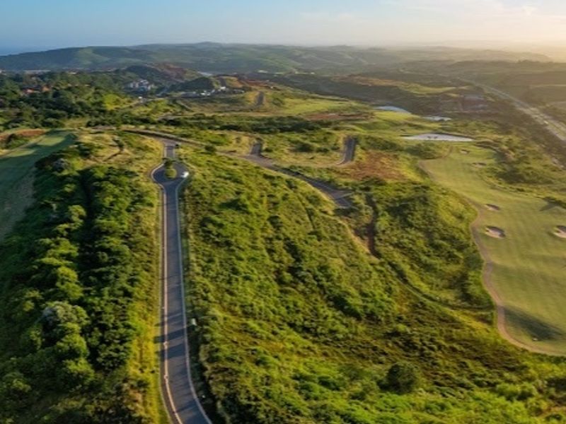 An aerial view of a residential estate featuring a paved road winding through landscaped hills and a golf course.