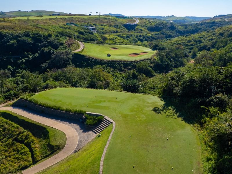 Aerial view of a well-maintained golf course fairway and green, featuring landscaped terrain, concrete pathways, and stone retaining walls.