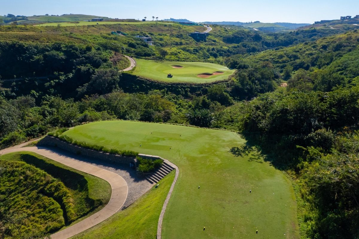 Aerial view of a well-maintained golf course fairway and green, featuring landscaped terrain, concrete pathways, and stone retaining walls.