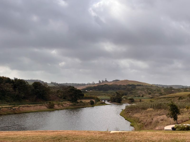 A scenic view of a natural water body surrounded by rolling hills and landscaped terrain, showcasing the peaceful landscape of the vacant land.