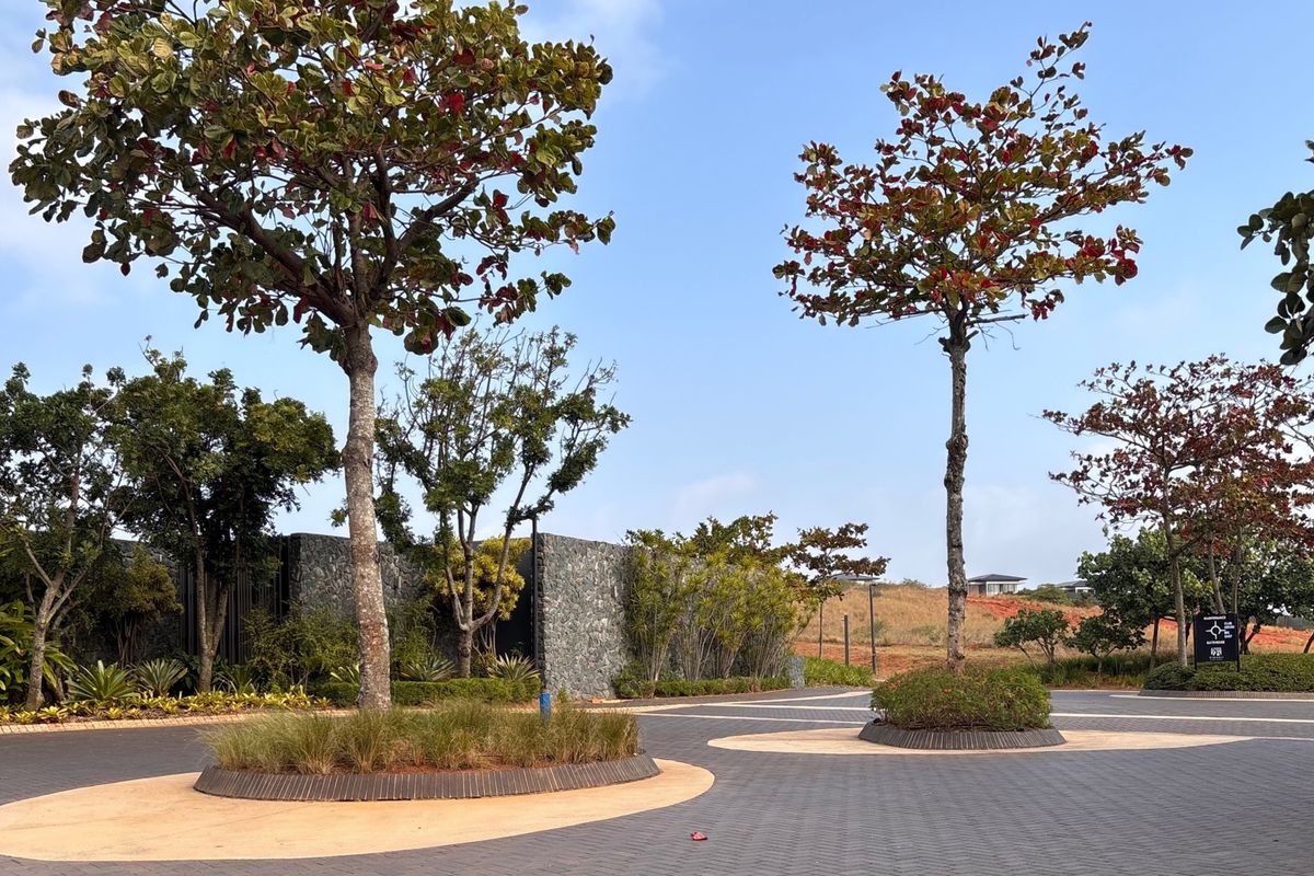 A well-maintained paved driveway entrance featuring landscaped tree islands and a stone retaining wall within a residential estate setting.