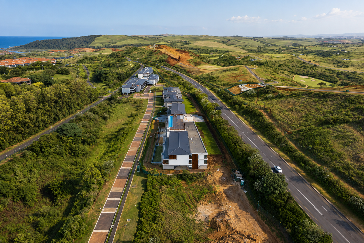 Aerial view of a modern apartment complex featuring a swimming pool, pitched roofs, and surrounding landscaped grounds near a main road.