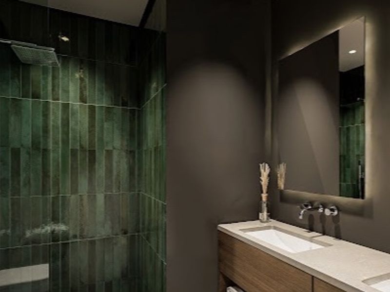 Modern luxury bathroom featuring a double vanity with wall-mounted faucets, backlit mirrors, and a spacious walk-in shower with dark green feature tiling.