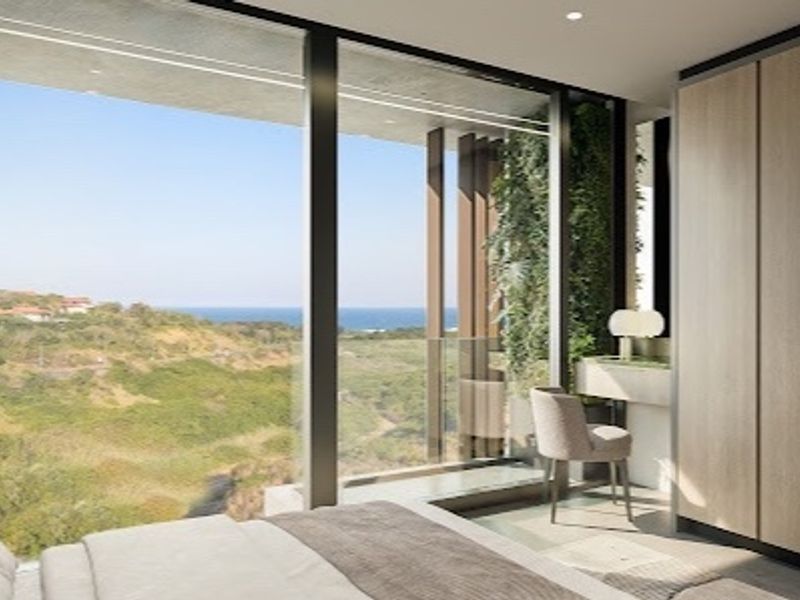 Modern bedroom featuring floor-to-ceiling windows with expansive coastal views, integrated built-in wardrobes, and high-end contemporary finishes.