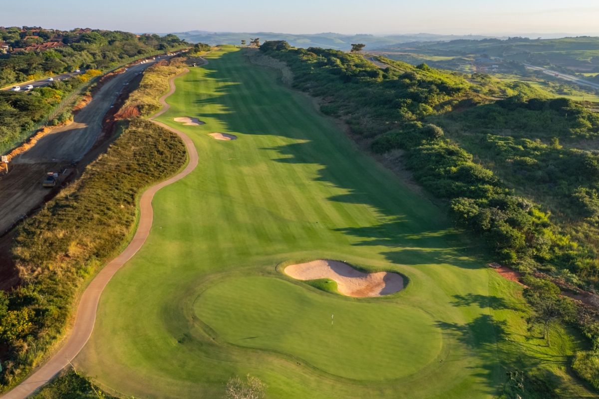 An aerial view of a well-maintained golf course fairway and green, showcasing the surrounding landscape and estate grounds.