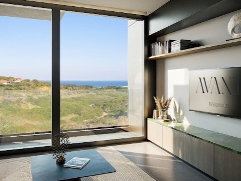 Modern living room featuring custom built-in cabinetry, floating shelves, and expansive floor-to-ceiling windows offering panoramic coastal views.