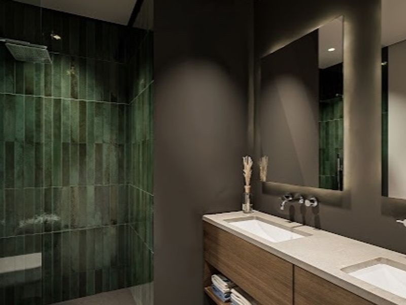 Modern luxury bathroom featuring a double vanity with integrated sinks, wall-mounted faucets, backlit mirrors, and a spacious walk-in shower with green feature tiling.