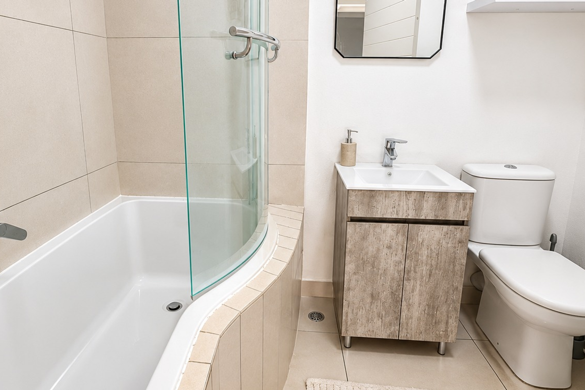 A modern bathroom featuring a curved shower screen over a bathtub, a wood-finish vanity cabinet with a basin, and a standard toilet.