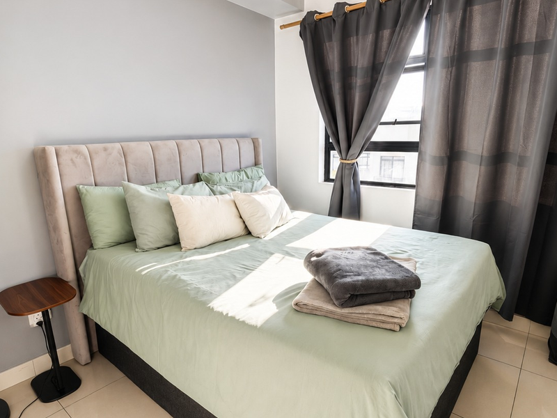 A well-lit bedroom featuring neutral wall tones, tiled flooring, and a window with installed curtain rods.