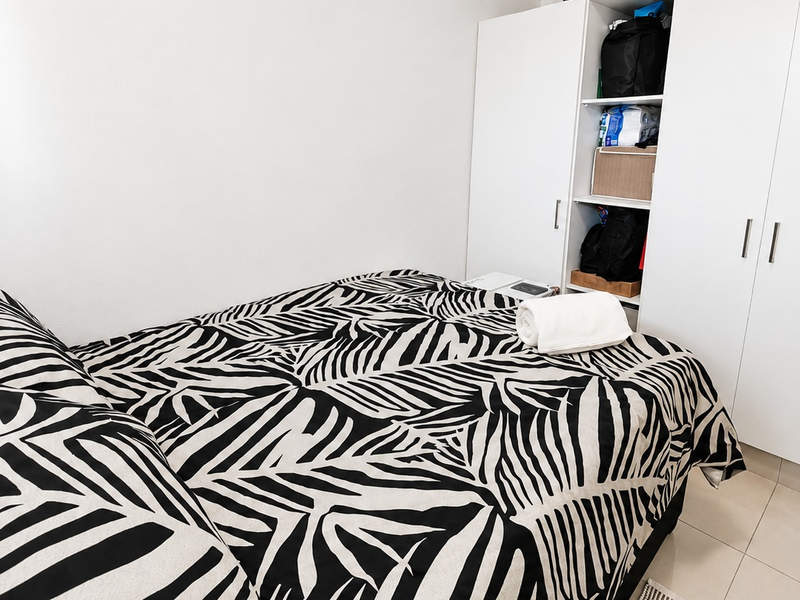 A compact bedroom featuring neutral tiled flooring and a functional white built-in wardrobe with integrated shelving.