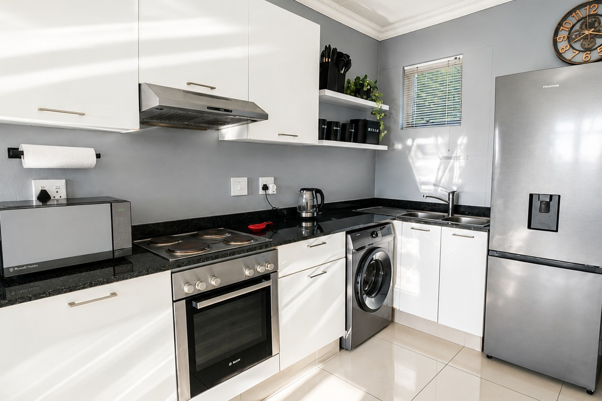 Modern kitchen featuring white cabinetry, granite countertops, built-in oven, electric hob, extractor fan, and integrated washing machine with tiled flooring.