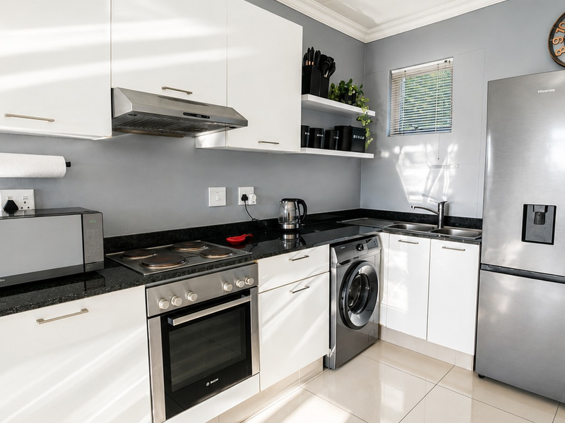 Modern kitchen featuring white cabinetry, granite countertops, built-in oven, electric hob, extractor fan, and integrated washing machine with tiled flooring.