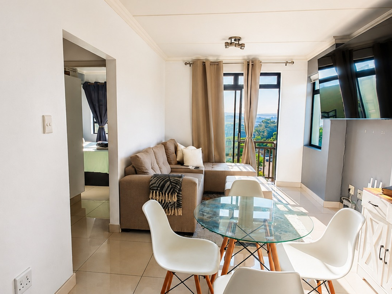 Bright open-plan living and dining area featuring tiled floors, modern finishes, and direct access to a balcony with scenic views.