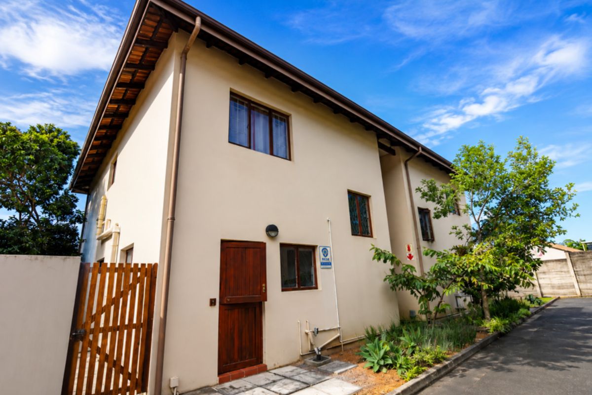 Rear exterior view of the townhouse featuring a timber door, paved walkway, and established garden area.