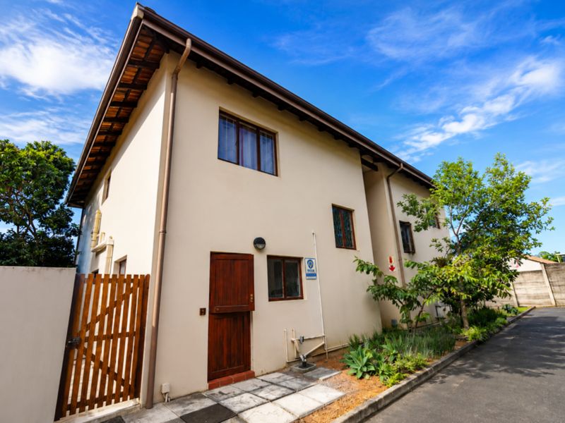 Rear exterior view of the townhouse featuring a timber door, paved walkway, and established garden area.