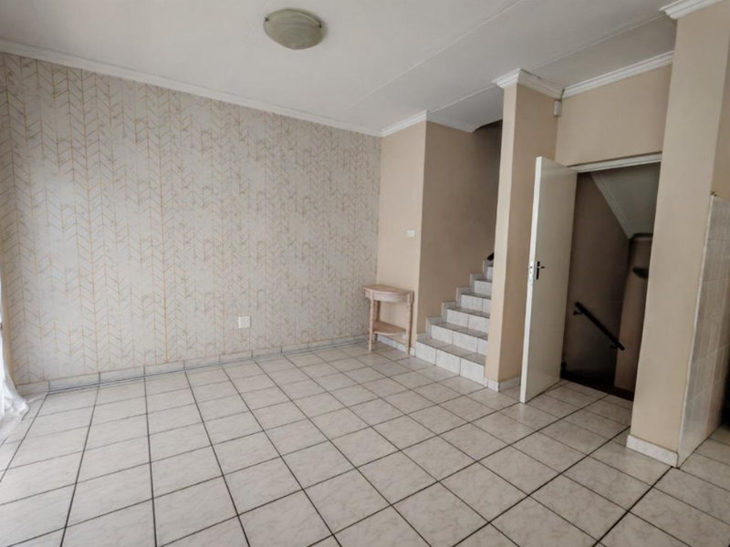 An empty living area featuring tiled flooring, a staircase leading to another level, and decorative wallpaper, offering a blank canvas for interior design.