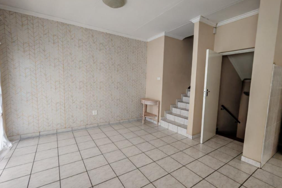 An empty living area featuring tiled flooring, a staircase leading to another level, and decorative wallpaper, offering a blank canvas for interior design.