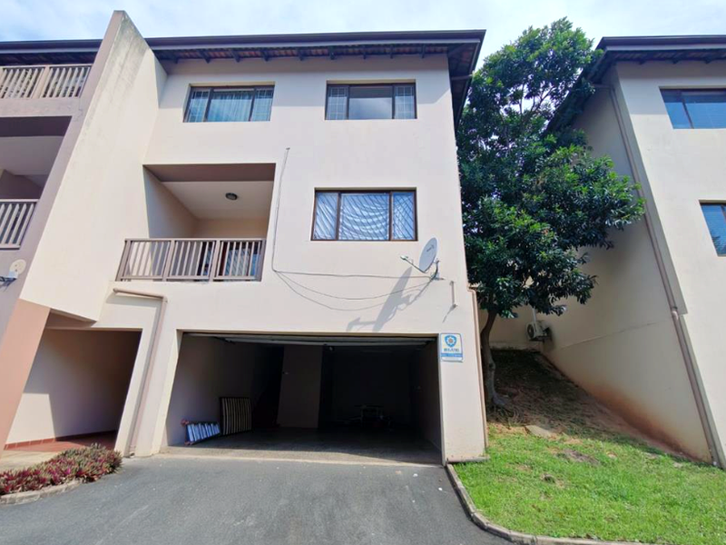 Front elevation of a multi-story townhouse featuring a ground-level garage, a private balcony, and a paved driveway area.