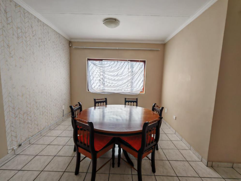 A functional dining room featuring tiled flooring, neutral wall tones, and a window with security bars, offering a blank canvas for modern interior updates.