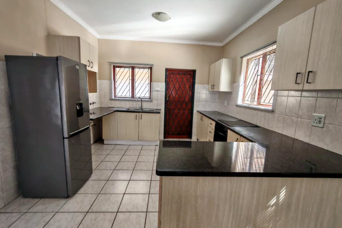 Functional kitchen featuring granite countertops, ample built-in cabinetry, tiled flooring, and security features on windows and the rear exit door.