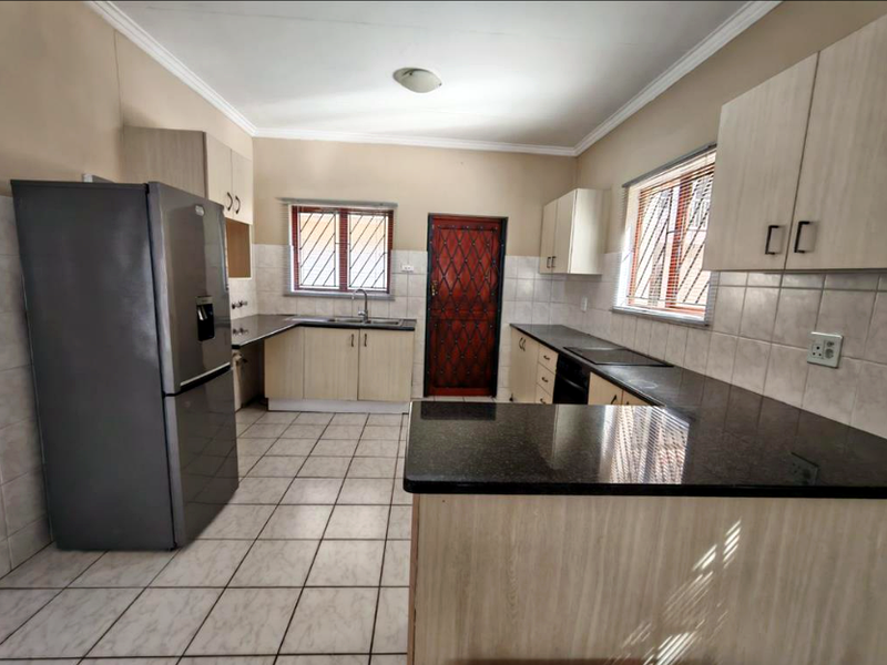 Functional kitchen featuring granite countertops, ample built-in cabinetry, tiled flooring, and security features on windows and the rear exit door.