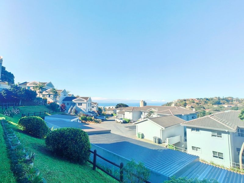 Elevated view overlooking a residential complex with well-maintained gardens, tiled roof structures, and distant coastal scenery.