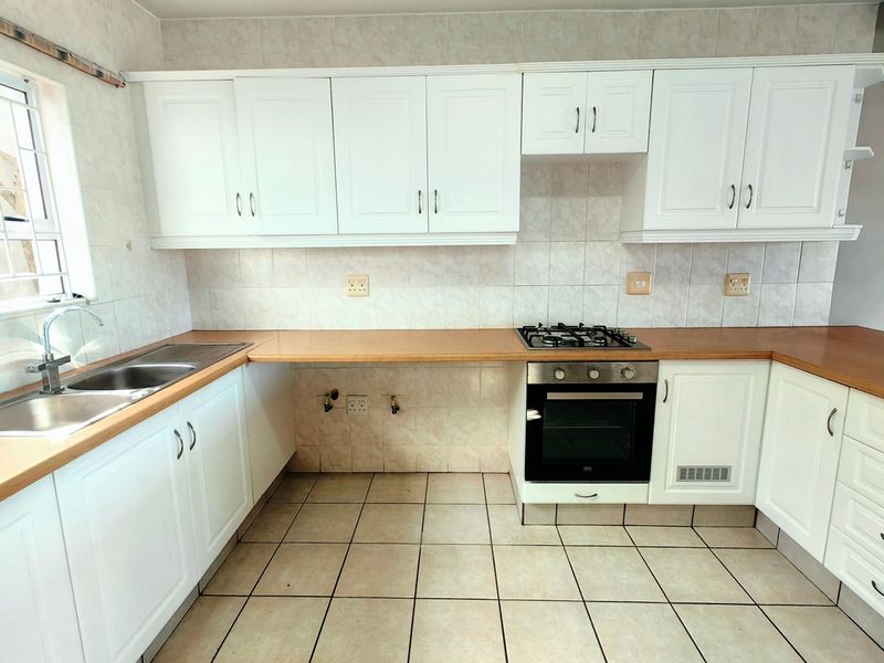 A functional kitchen featuring white cabinetry, laminate countertops, a gas hob, built-in oven, and tiled flooring with a neutral backsplash.