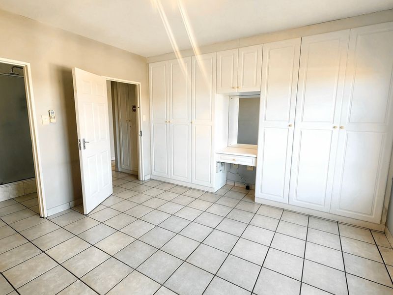 Spacious bedroom featuring extensive built-in cabinetry with an integrated vanity station, tiled flooring, and direct access to an en-suite bathroom.