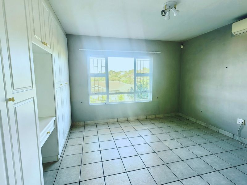 An empty bedroom featuring tiled flooring, built-in cupboards with a vanity section, and a wall-mounted air conditioning unit.