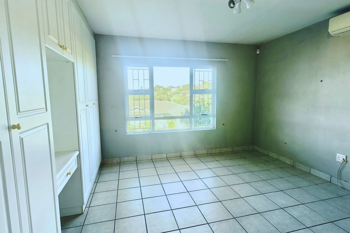 An empty bedroom featuring tiled flooring, built-in cupboards with a vanity section, and a wall-mounted air conditioning unit.