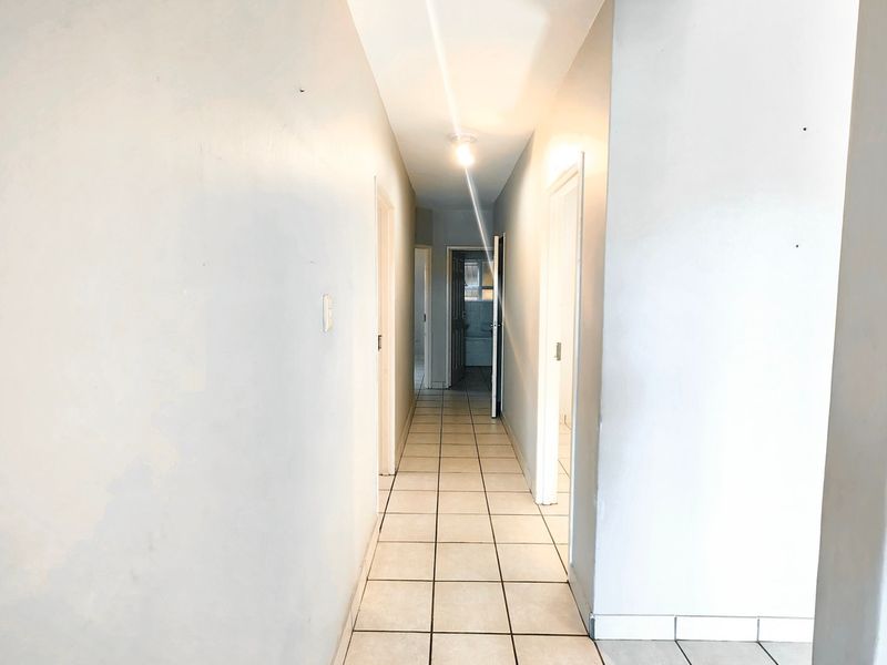 A bright, empty hallway featuring neutral wall paint and ceramic floor tiles, providing access to multiple rooms within the apartment.