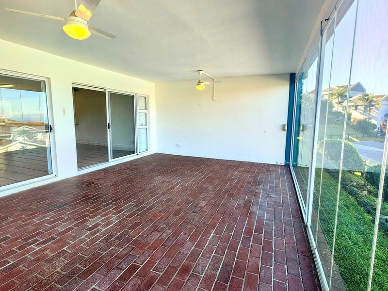 A spacious enclosed balcony featuring brick flooring, ceiling fans, and large sliding glass doors, offering a versatile outdoor living area.