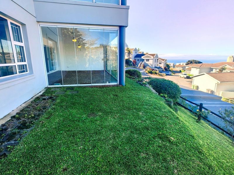 Rear view of the apartment featuring a glass-enclosed patio, upper balcony, and a well-maintained sloped lawn overlooking the neighborhood.