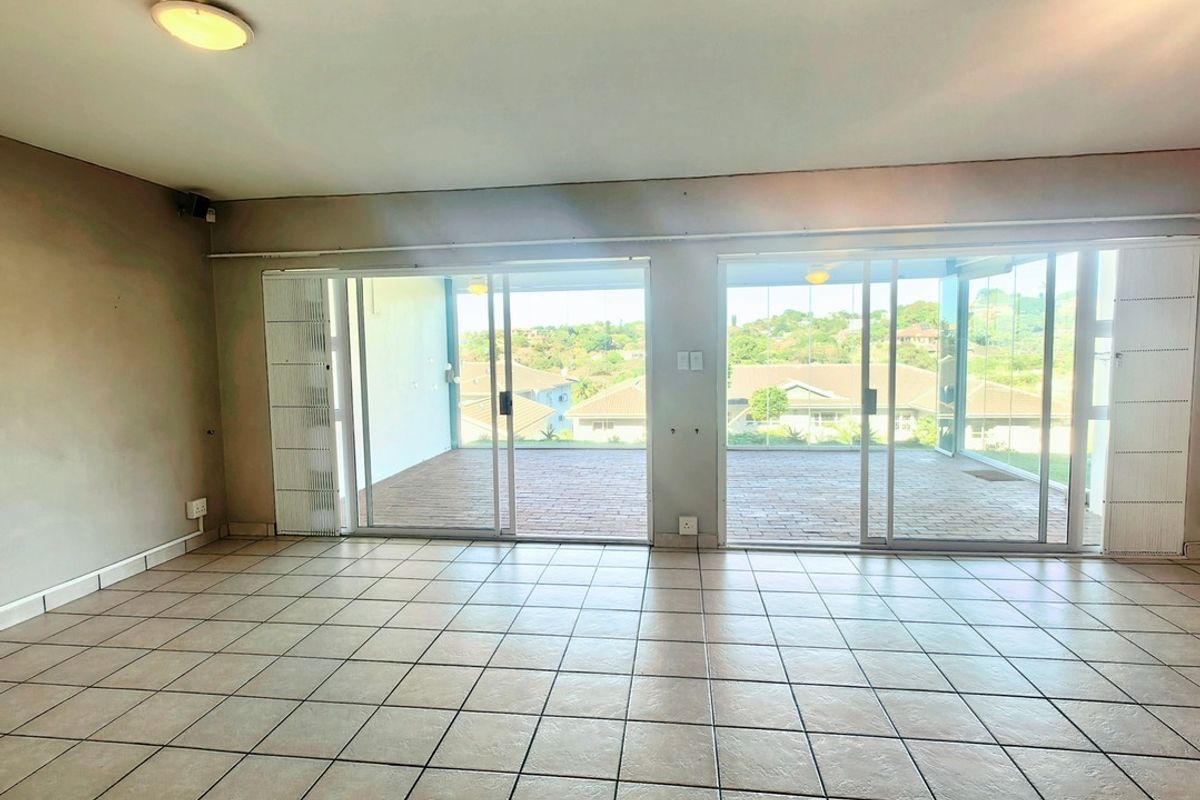 Spacious, empty living area featuring neutral tiled flooring and large sliding glass doors that open onto a covered balcony with scenic views.