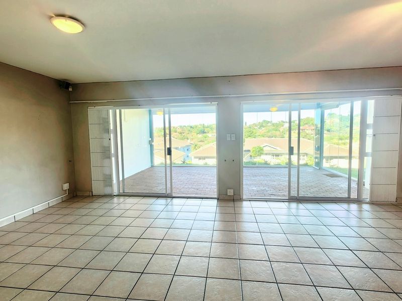Spacious, empty living area featuring neutral tiled flooring and large sliding glass doors that open onto a covered balcony with scenic views.