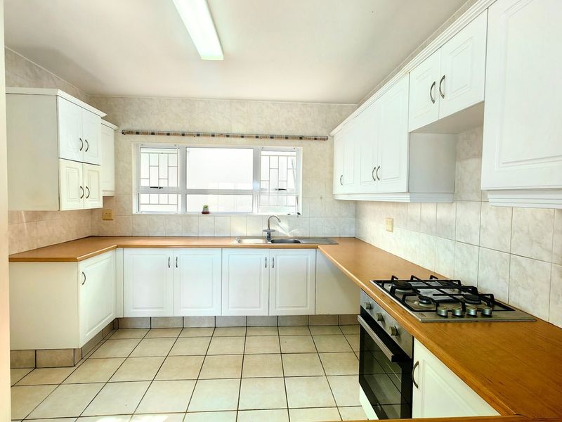 A functional kitchen featuring white cabinetry, laminate countertops, a gas hob, built-in oven, and tiled flooring with ample natural light.