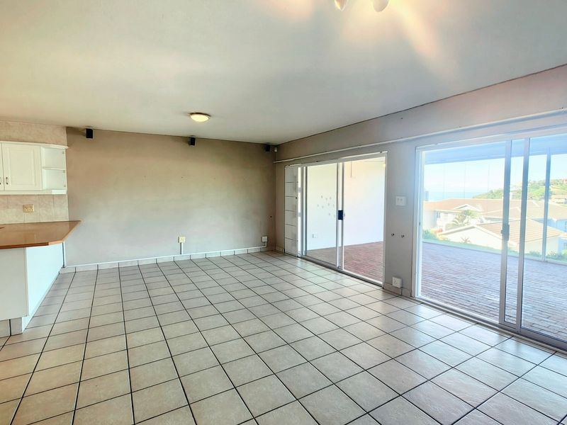 Spacious open-plan living area featuring tiled floors, kitchen cabinetry, and large sliding glass doors leading to an outdoor balcony with scenic views.