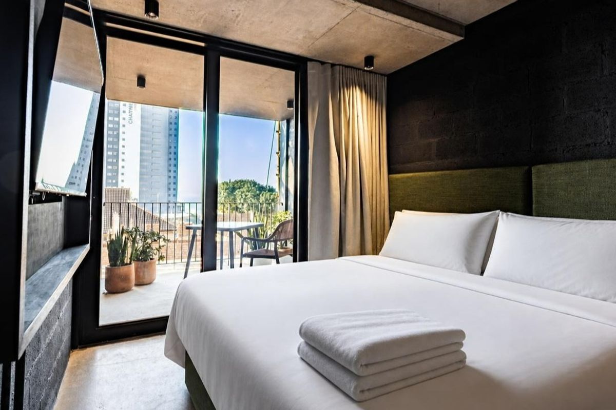 Modern bedroom featuring an exposed concrete ceiling, dark brick feature wall, and large sliding glass doors opening onto a private balcony.
