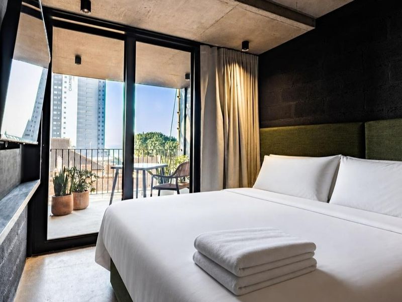 Modern bedroom featuring an exposed concrete ceiling, dark brick feature wall, and large sliding glass doors opening onto a private balcony.