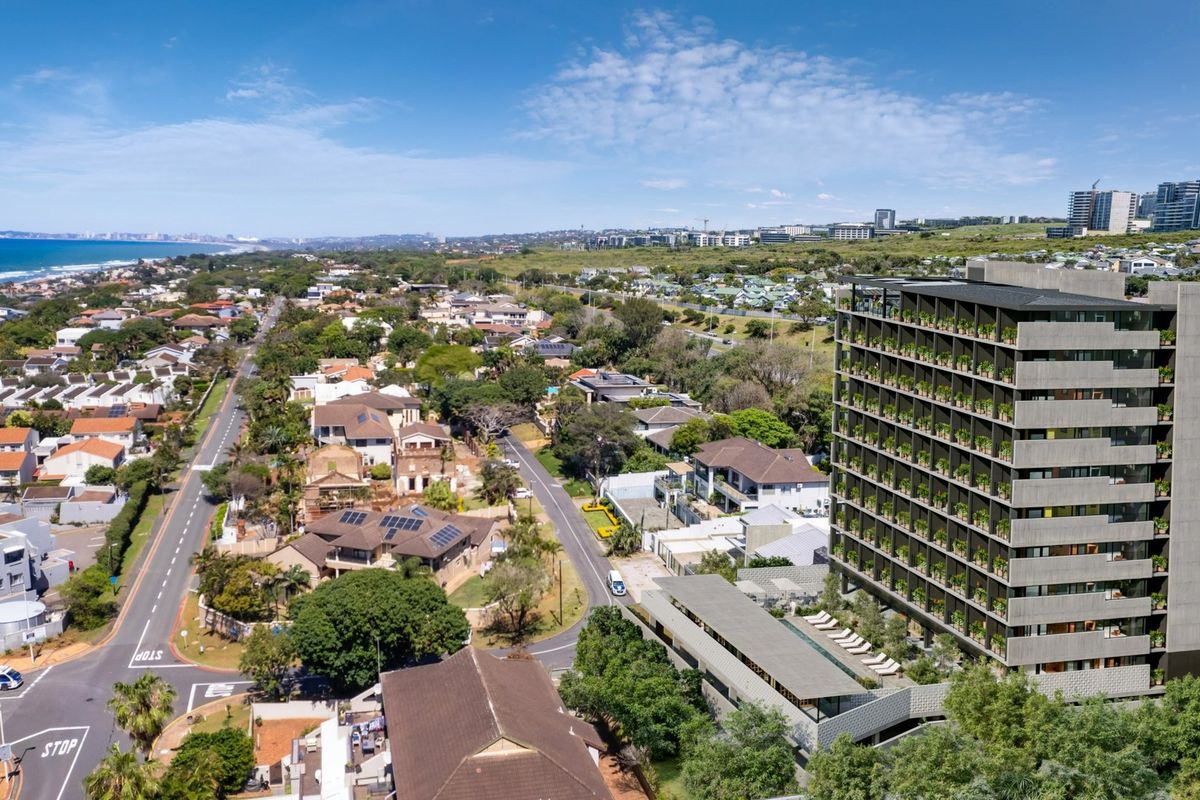 Aerial view of a modern multi-story apartment complex featuring a swimming pool and landscaped surroundings in a coastal neighborhood setting.