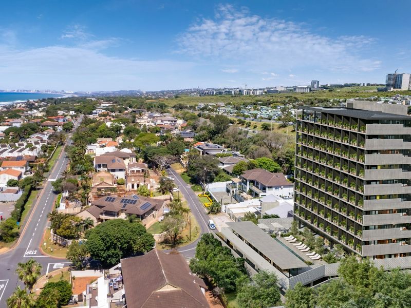 Aerial view of a modern multi-story apartment complex featuring a swimming pool and landscaped surroundings in a coastal neighborhood setting.