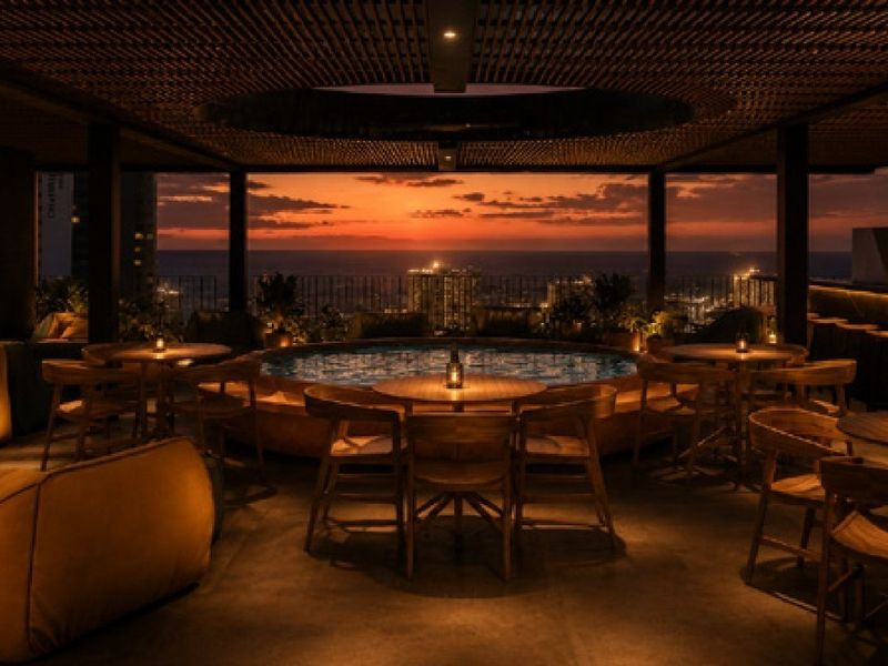 A sophisticated rooftop pool area featuring a built-in pool, slatted timber ceiling, and panoramic sunset views over the city skyline.