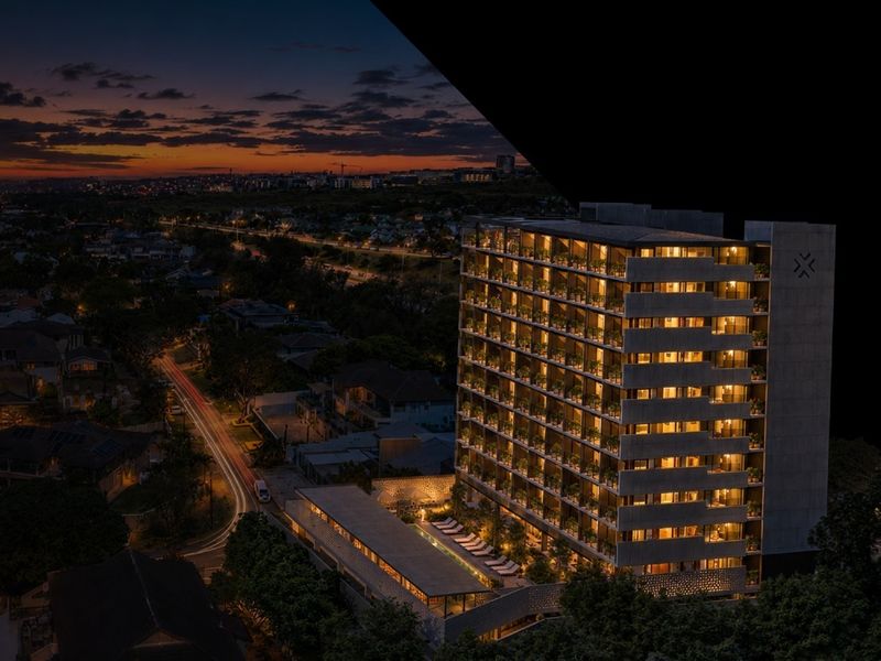 Aerial night view of a modern multi-story apartment complex featuring a swimming pool and illuminated balconies set against a city landscape.