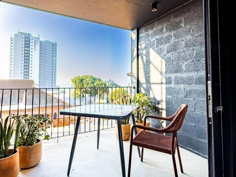 A modern balcony featuring exposed concrete block walls, a metal railing, and a concrete floor, offering an open-air space with urban views.